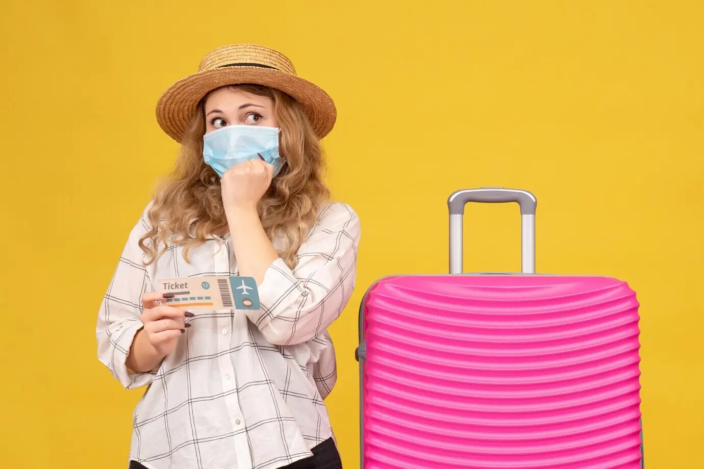Vorderansicht einer nachdenklichen jungen Frau mit Maske, die ein Ticket zeigt und neben ihrer pinken Tasche steht, auf gelbem Grund.